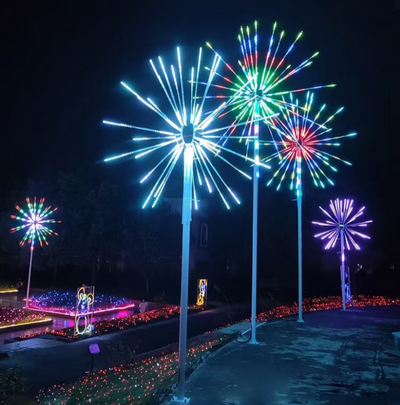 Colorful RGB DMX fireworks light installation with animated LED bursts in blue, red, green, and purple on tall poles, featured in a landscaped nighttime display
